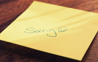 Yellow stick note with the word "sorry" and smiley face written in pen.